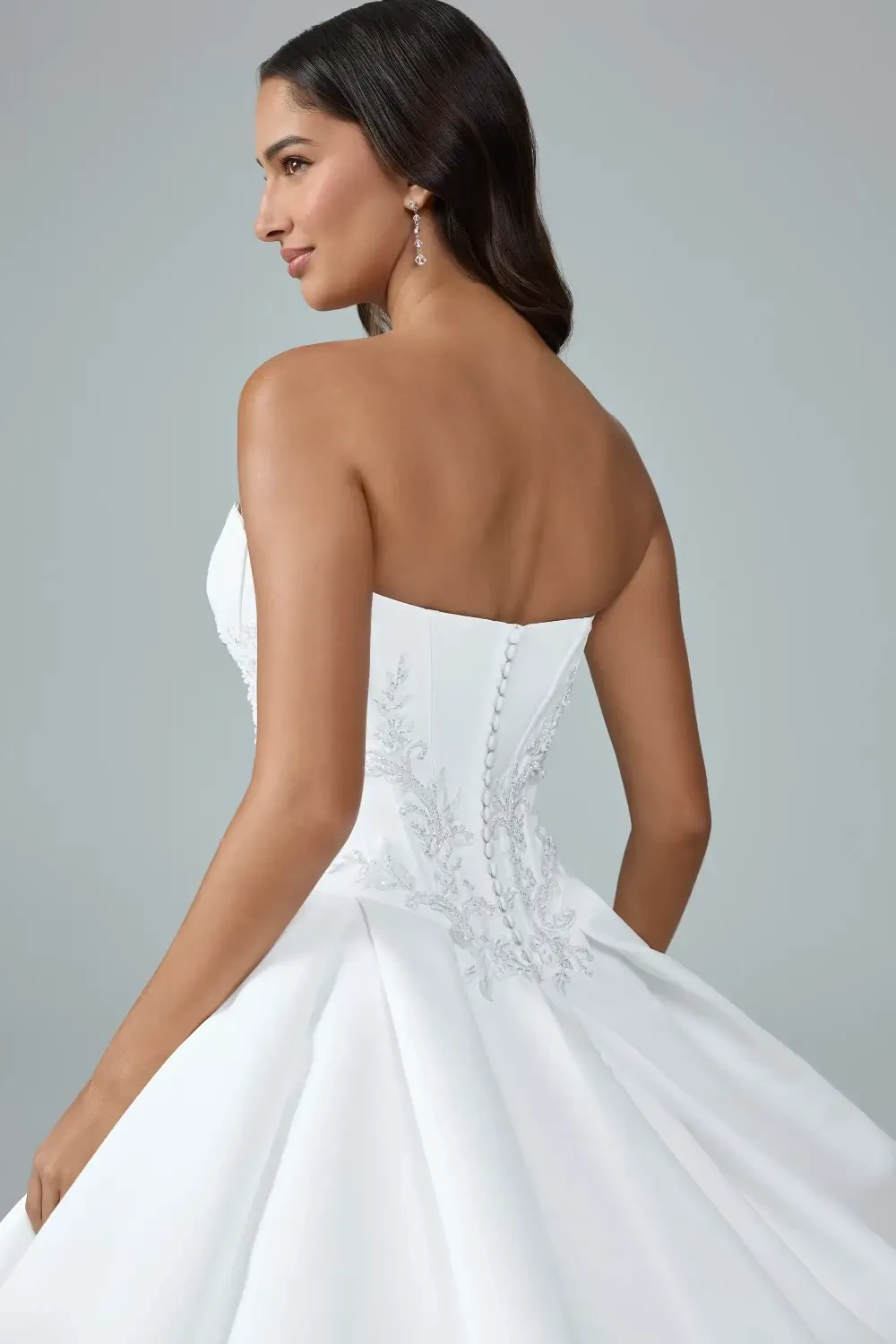 A woman in a strapless white wedding dress with a full skirt, standing outdoors with greenery in the background.