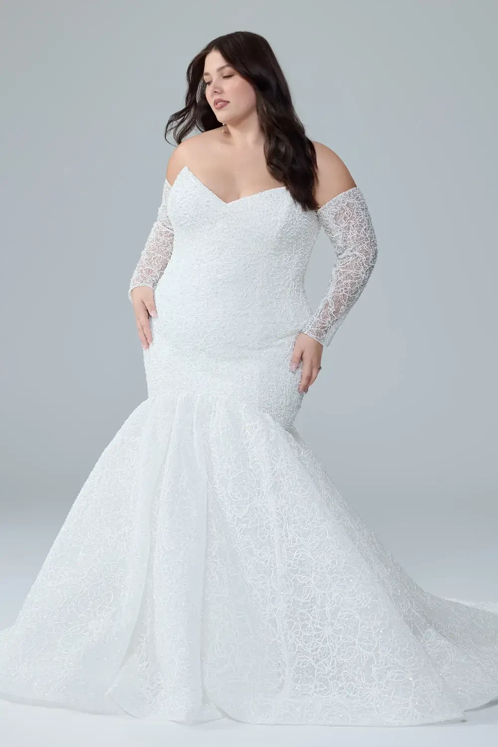 A model wearing a fitted white lace wedding dress with off-the-shoulder sleeves and a mermaid silhouette.