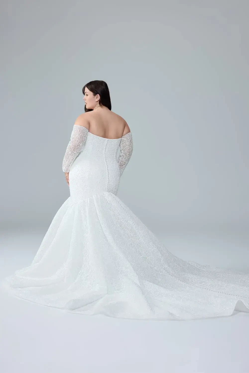 A model wearing a fitted white lace wedding dress with off-the-shoulder sleeves and a mermaid silhouette.