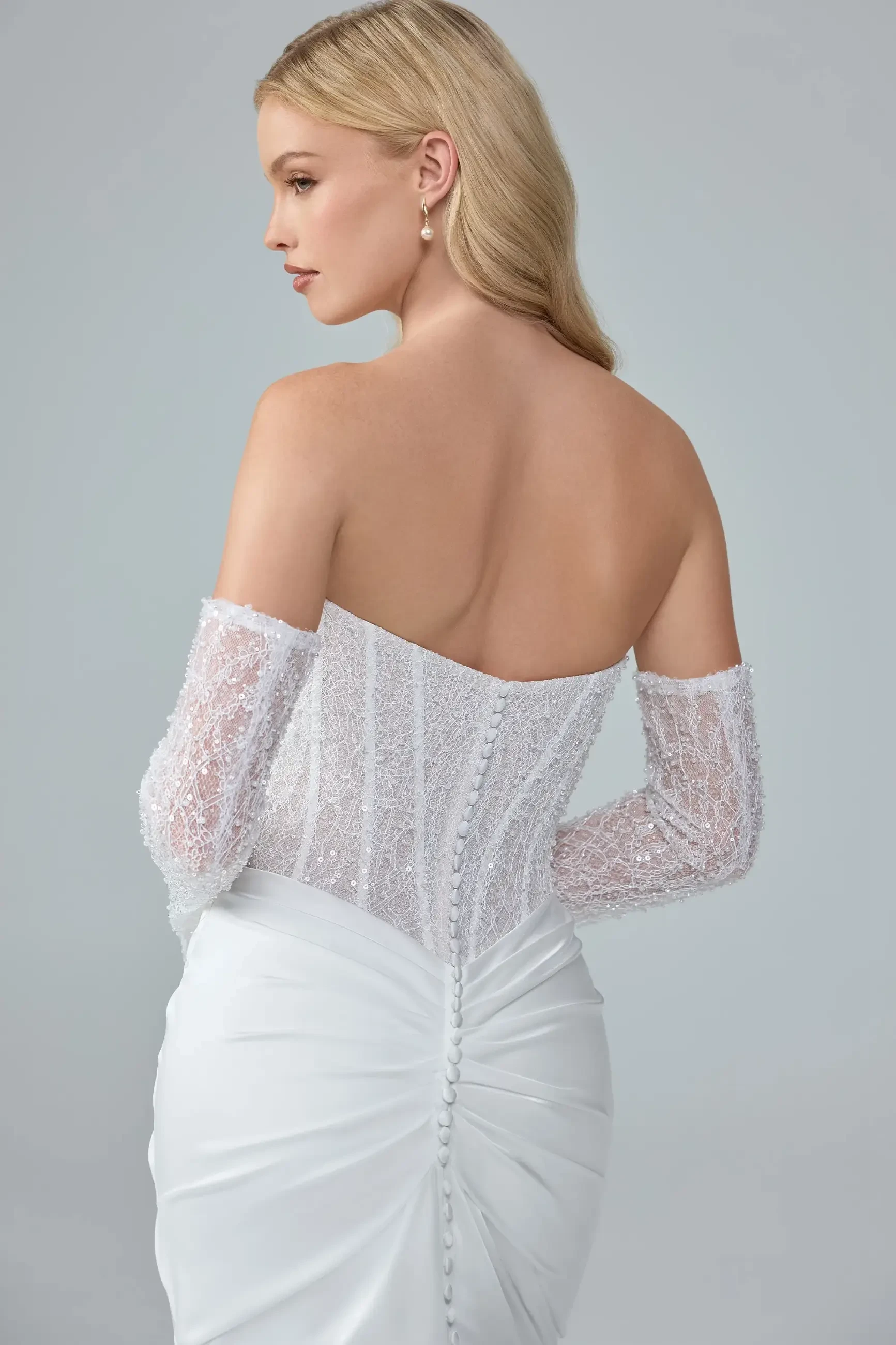 A woman wearing an elegant off-the-shoulder white gown with lace sleeves, shown from the back.