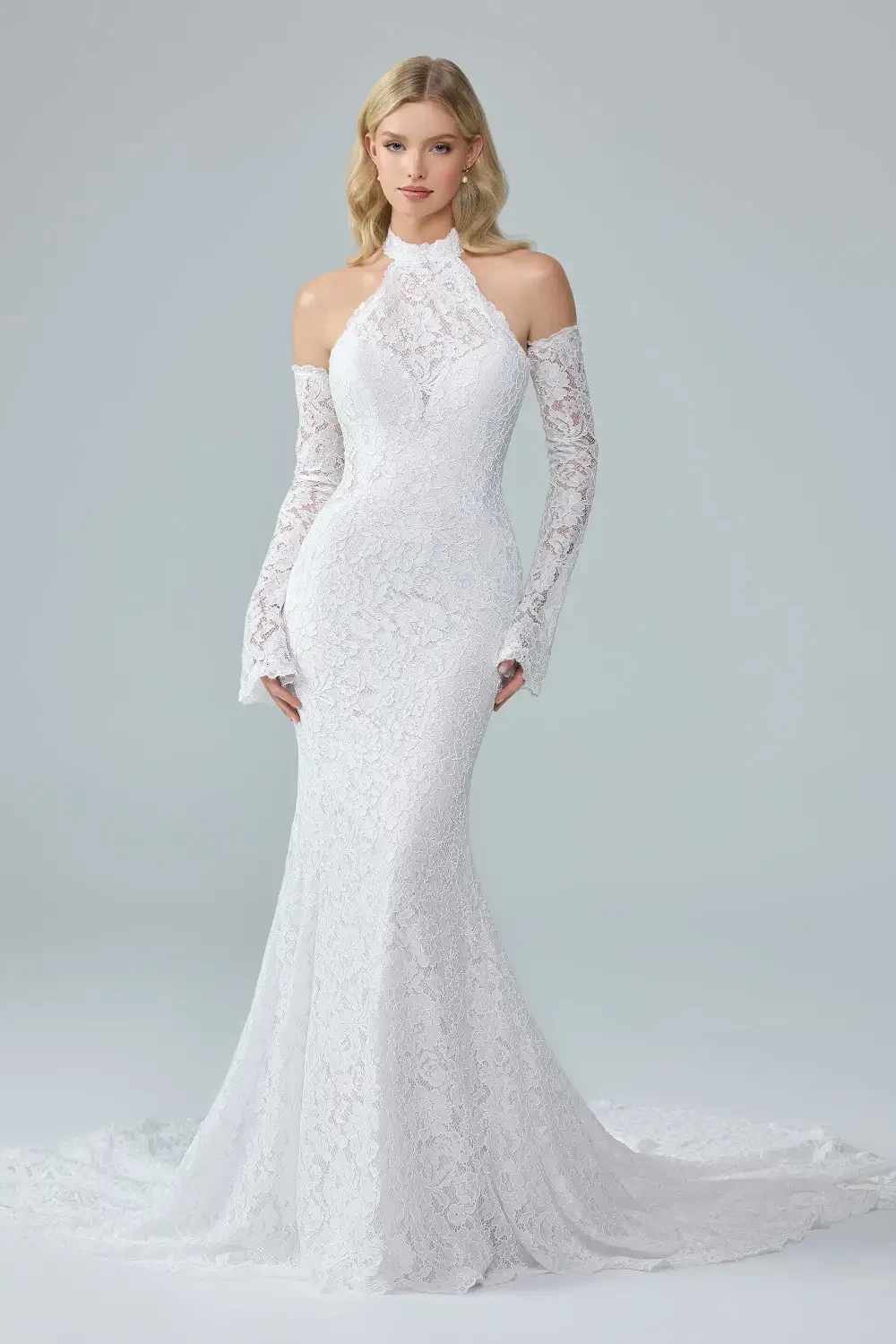 A model wearing a form-fitting white lace gown with off-the-shoulder long sleeves, standing against a light gray background.